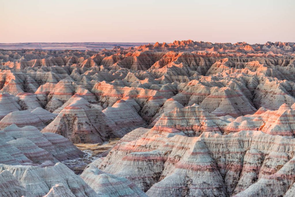 Uitgestrekt landschap van gestreepte rotsformaties en pieken in zachte pastelkleuren tijdens zonsondergang in Badlands National Park