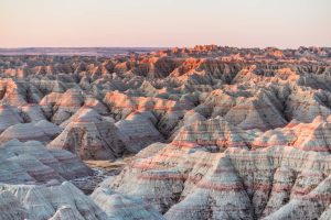 Uitgestrekt landschap van gestreepte rotsformaties en pieken in zachte pastelkleuren tijdens zonsondergang in Badlands National Park