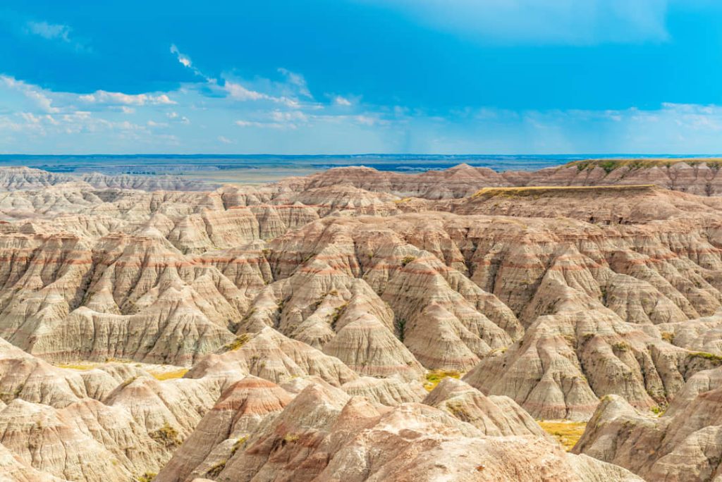 Wijds uitzicht over de gestreepte, geërodeerde rotsformaties van de Badlands onder een blauwe lucht met wolken in South Dakota