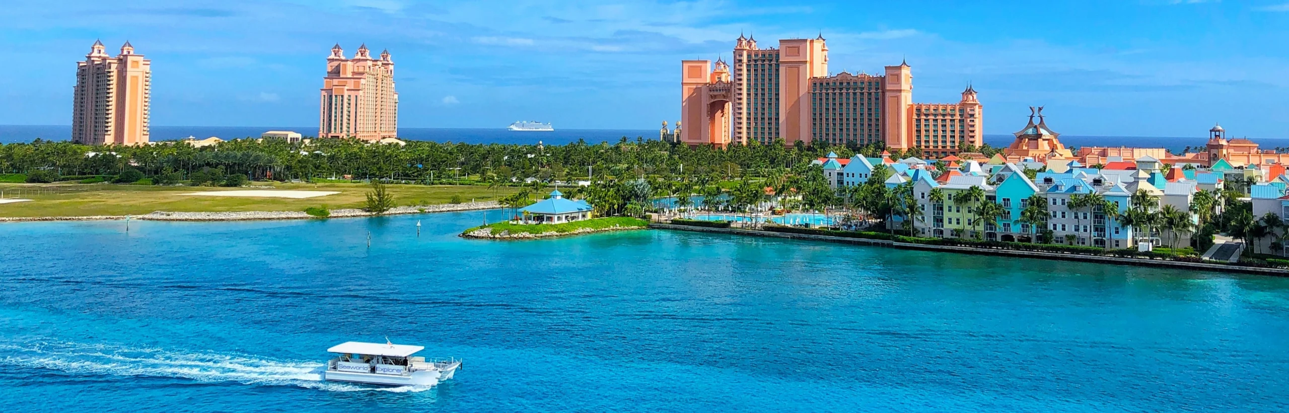 Uitzicht over turkooisblauw water bij Nassau op de Bahama's met roze resorttorens, palmbomen en een rondvaartboot