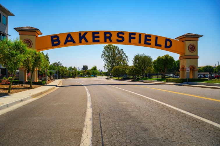 Gele boog met de tekst Bakersfield overspant een lege weg tussen bomen onder een strakblauwe lucht