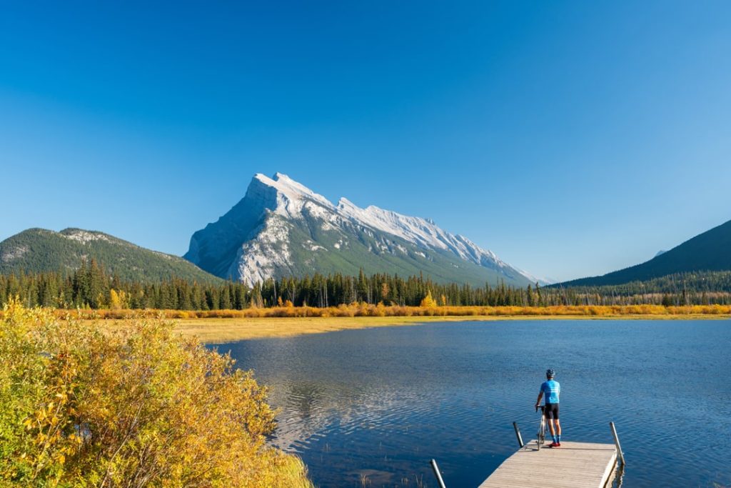Fietser staat op een steiger bij de Vermilion Lakes met uitzicht op de kartelige top van Mount Rundle