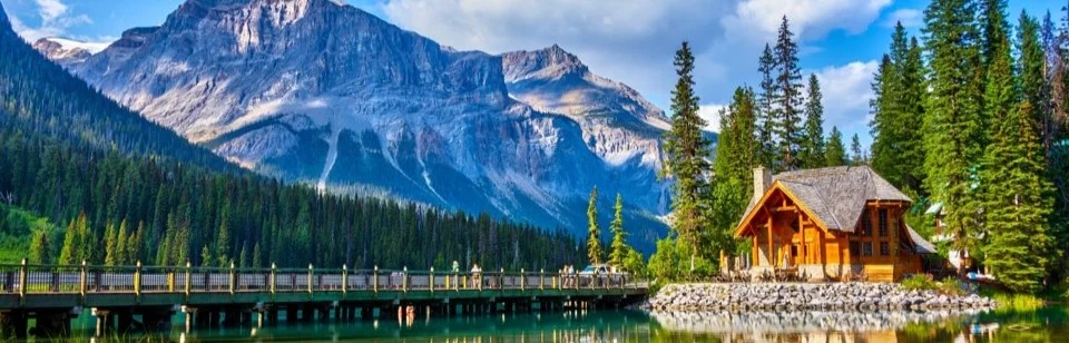 Een houten lodge met brug over turquoise water bij Emerald Lake in Banff National Park, omringd door dennenbossen en besneeuwde bergtoppen