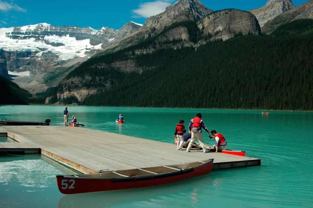 Kinderen met zwemvesten helpen een rode kano de steiger op bij het turquoise water van Lake Louise, met bergen op de achtergrond