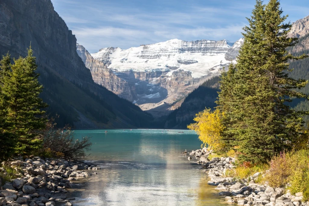Turquoise water van Lake Louise omringd door dennenbomen, met een besneeuwde bergketen en gletsjer op de achtergrond