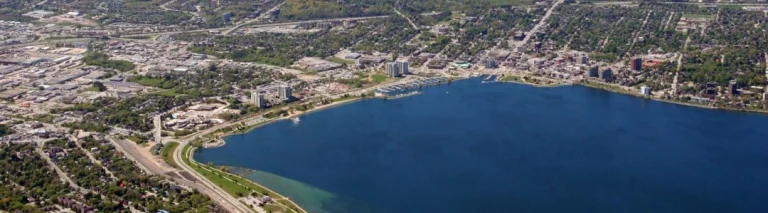 Luchtfoto van de stad Barrie met gebouwen en een spoorlijn langs de blauwe oever van het meer