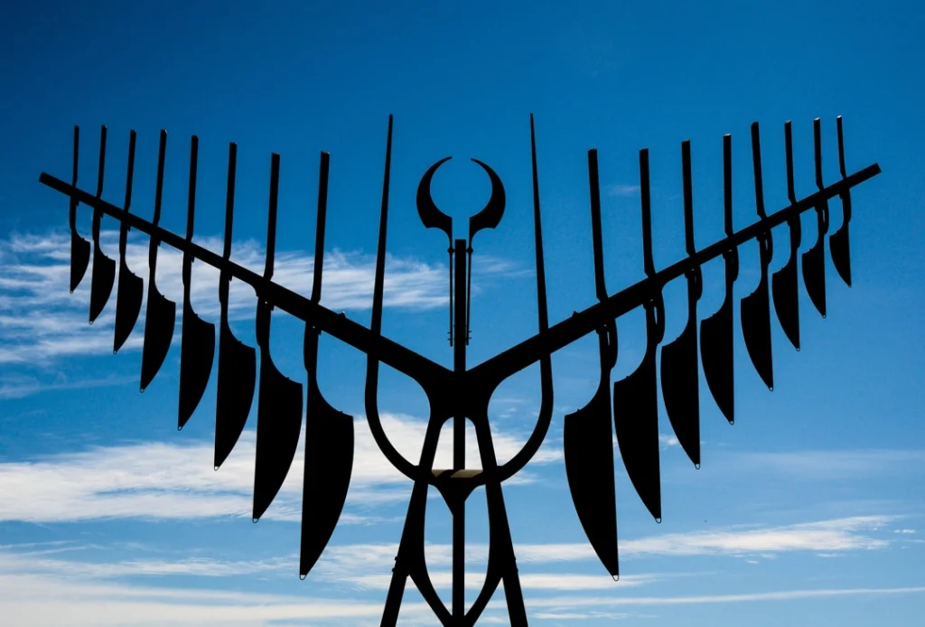 Zwart metalen kunstwerk in de vorm van gespreide vleugels tegen een strakke blauwe hemel met wolken in Barrie