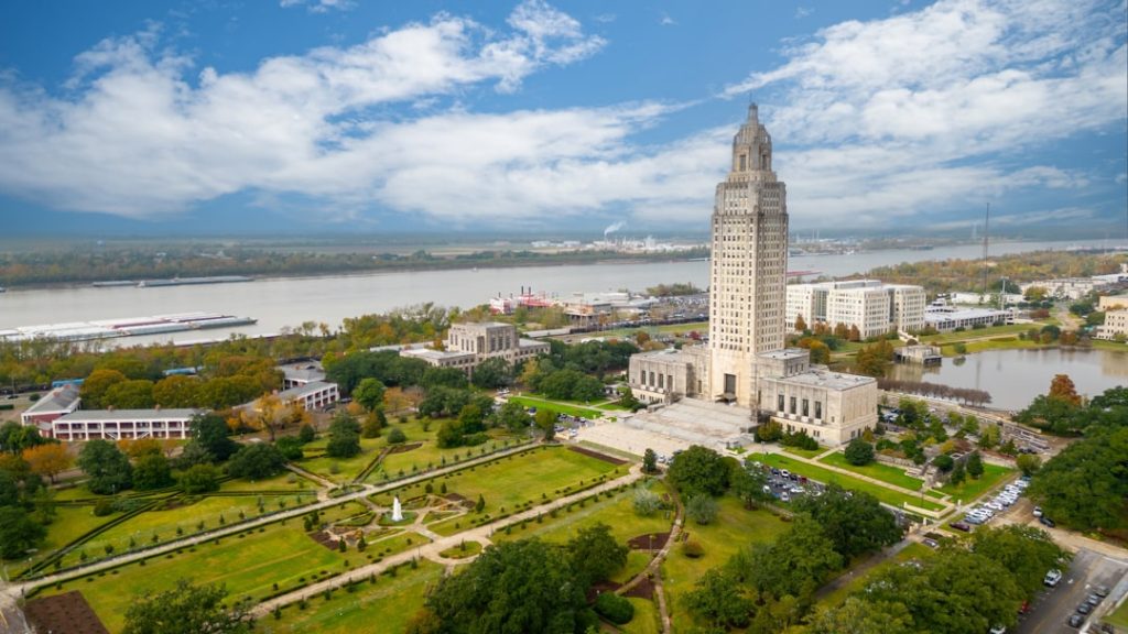 Luchtfoto van de hoge witte toren van het Louisiana State Capitol omringd door tuinen met de Mississippi rivier op de achtergrond in Baton Rouge