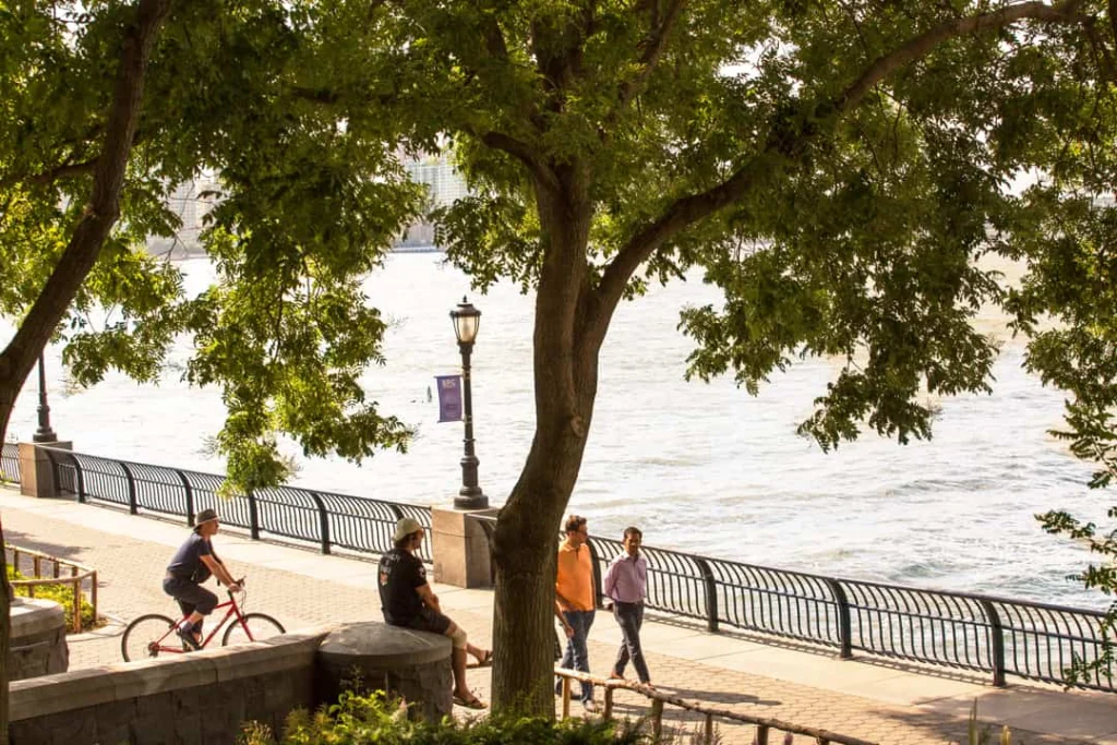 Mensen wandelen en fietsen over het schaduwrijke pad langs het water in Battery Park in New York