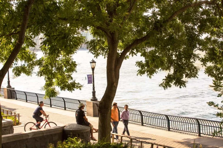 Mensen wandelen en fietsen over het schaduwrijke pad langs het water in Battery Park in New York