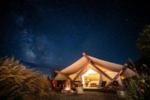 Verlichte glampingtent met kampvuur ervoor onder een heldere sterrenhemel met de Melkweg zichtbaar