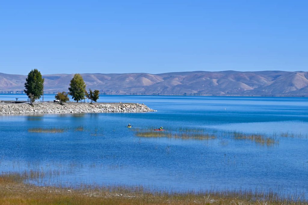 Rustige oever van Bear Lake met bomen op een rotspunt en twee kanoërs op het kalme blauwe water, heuvels aan de horizon