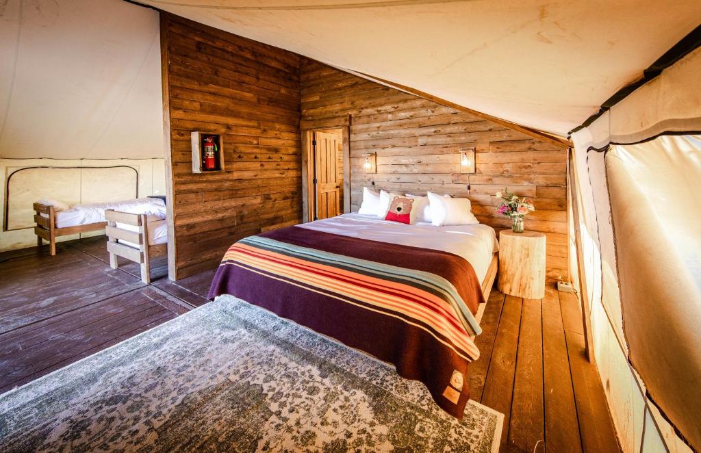 Rustieke slaapkamer in een glampingtent met houten wanden, een tweepersoonsbed met gestreepte deken en een stapelbed op de achtergrond