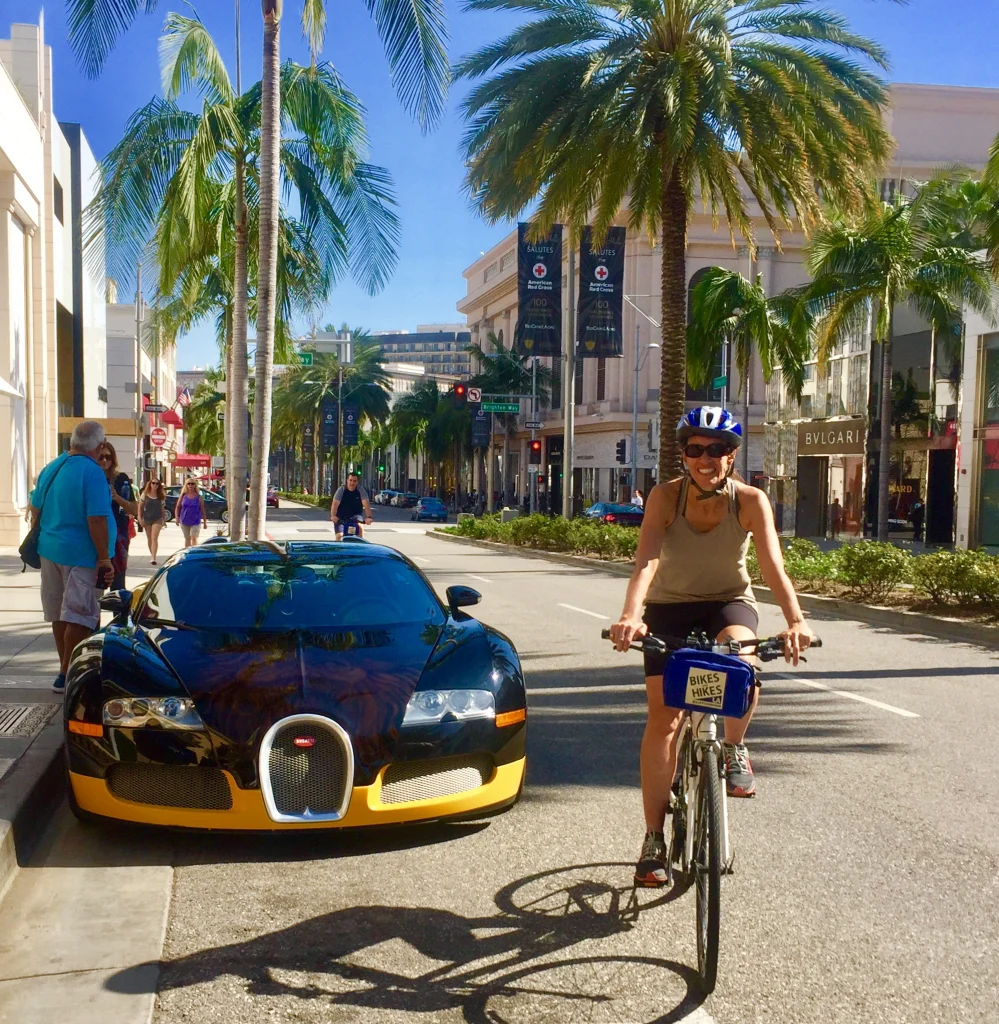 Vrouw op een fiets met helm rijdt langs een gele en zwarte Bugatti sportwagen op de palmbomenlaan Rodeo Drive