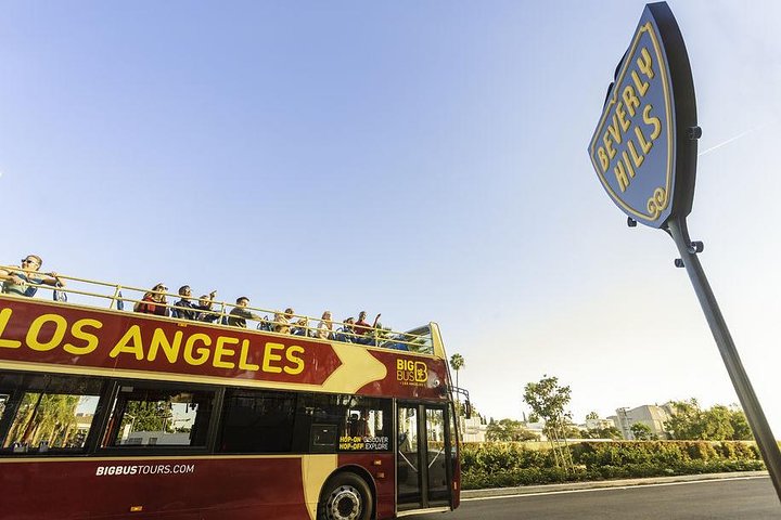 Open sightseeingbus vol toeristen rijdt voorbij het bekende blauwe plaatsnaambord van Beverly Hills bij Los Angeles