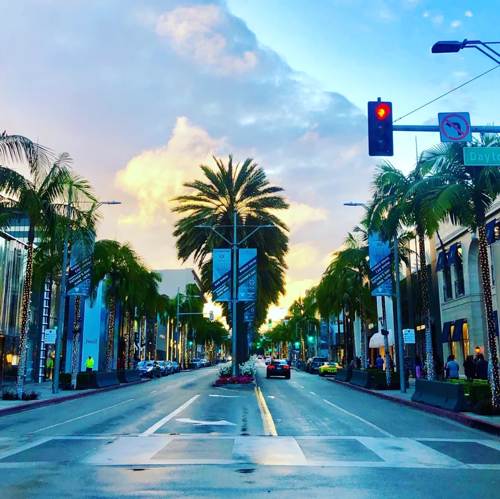 Lege winkelstraat Rodeo Drive met hoge palmbomen en luxe winkels in Beverly Hills onder een kleurrijke avondlucht