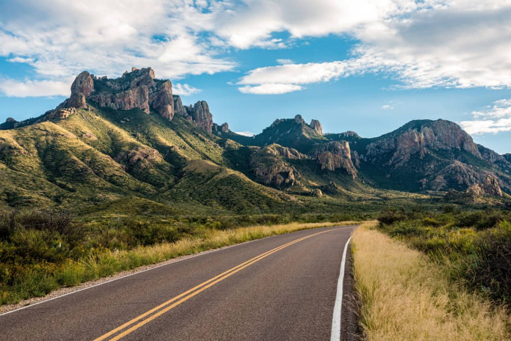 Lege asfaltweg met dubbele gele lijn voert door grasland richting de ruige pieken van de Chisos Mountains in Big Bend