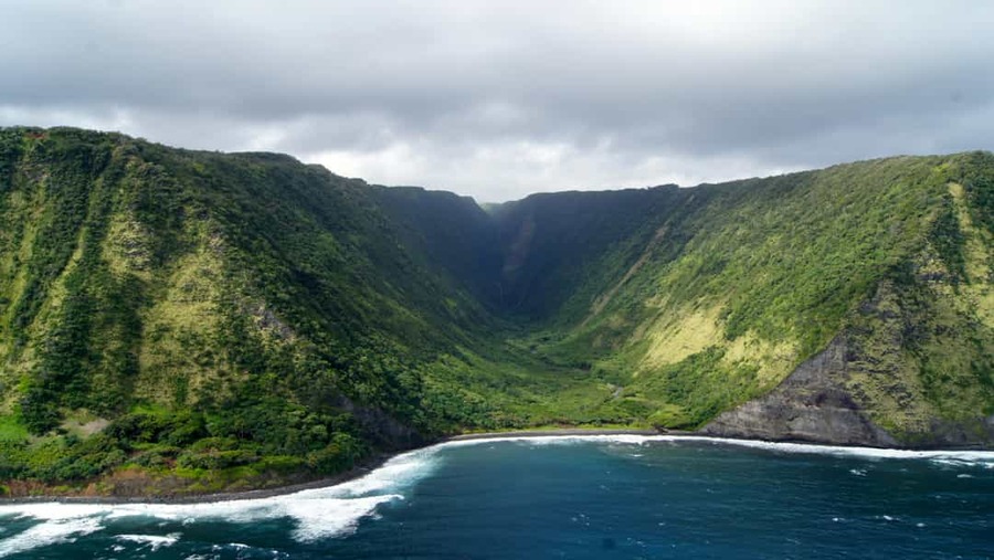 Luchtfoto van een diepe groene vallei omringd door steile begroeide kliffen die uitkomt op een baai met blauw water op Big Island