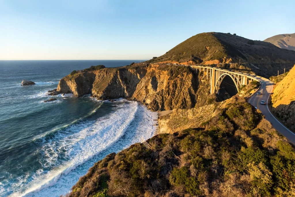 Luchtfoto van de Bixby Bridge met een rijdende auto, uitkijkend over de kliffen en het strand van Big Sur