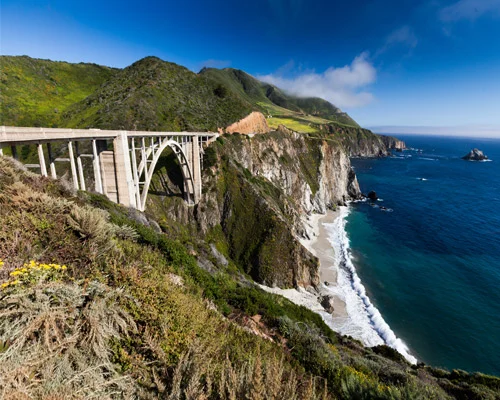 Witte stenen brug over een diep ravijn met uitzicht op de oceaan en een verlaten strand in Big Sur