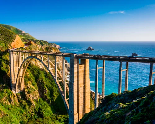 Gebogen betonnen brug overspant een groene kloof met uitzicht op de blauwe oceaan bij Big Sur in Californië