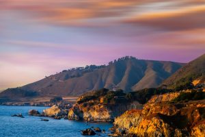 Paarsroze zonsondergang boven de rotsachtige kustlijn en glooiende heuvels van Big Sur aan de West-Amerikaanse kust