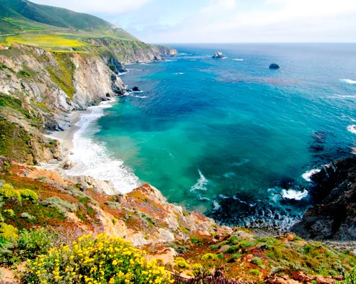Steile groene kliffen omzomen een turquoise baai met rotsen in zee langs de kust van Big Sur in Californië