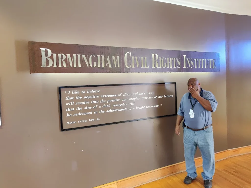 Een gids staat in Birmingham bij een wandbord met de tekst Birmingham Civil Rights Institute en een citaat van Martin Luther King Jr
