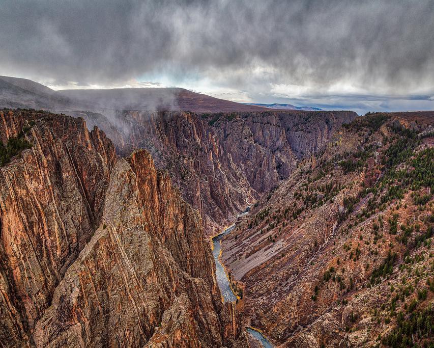 Steile donkere rotswanden van de Black Canyon of the Gunnison in Colorado met een rivier op de bodem en lage wolken erboven