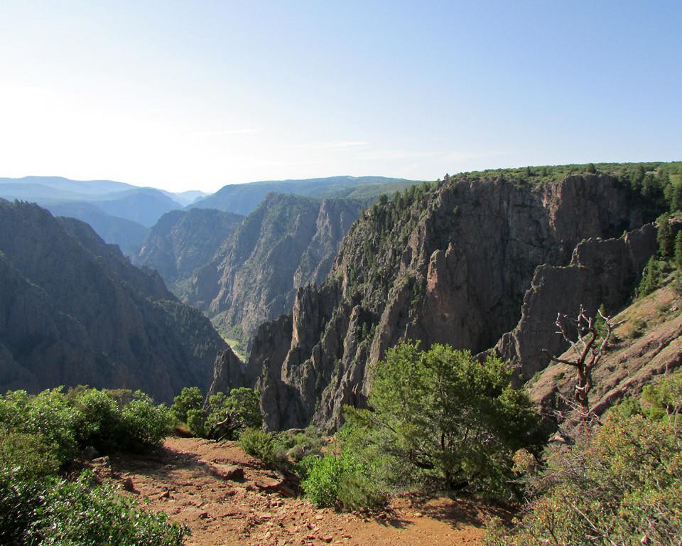 Wandelpad langs de rand van de Black Canyon of the Gunnison in Colorado met uitzicht op scherpe rotspieken en begroeide hellingen