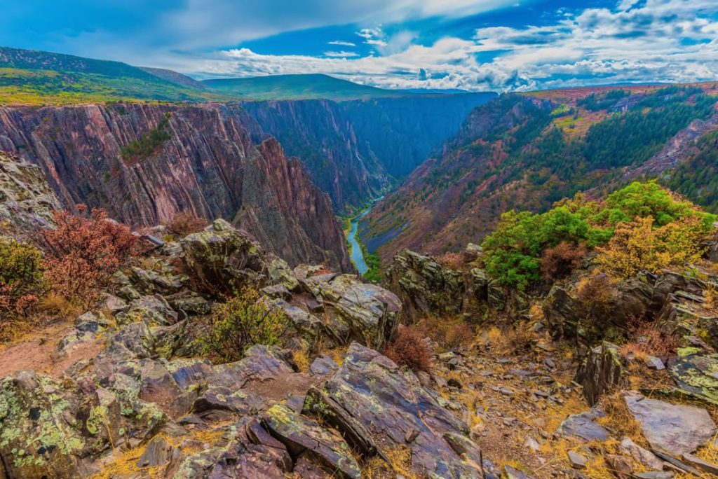 Steile donkere rotswanden dalen af naar een rivier diep op de bodem van Black Canyon of the Gunnison