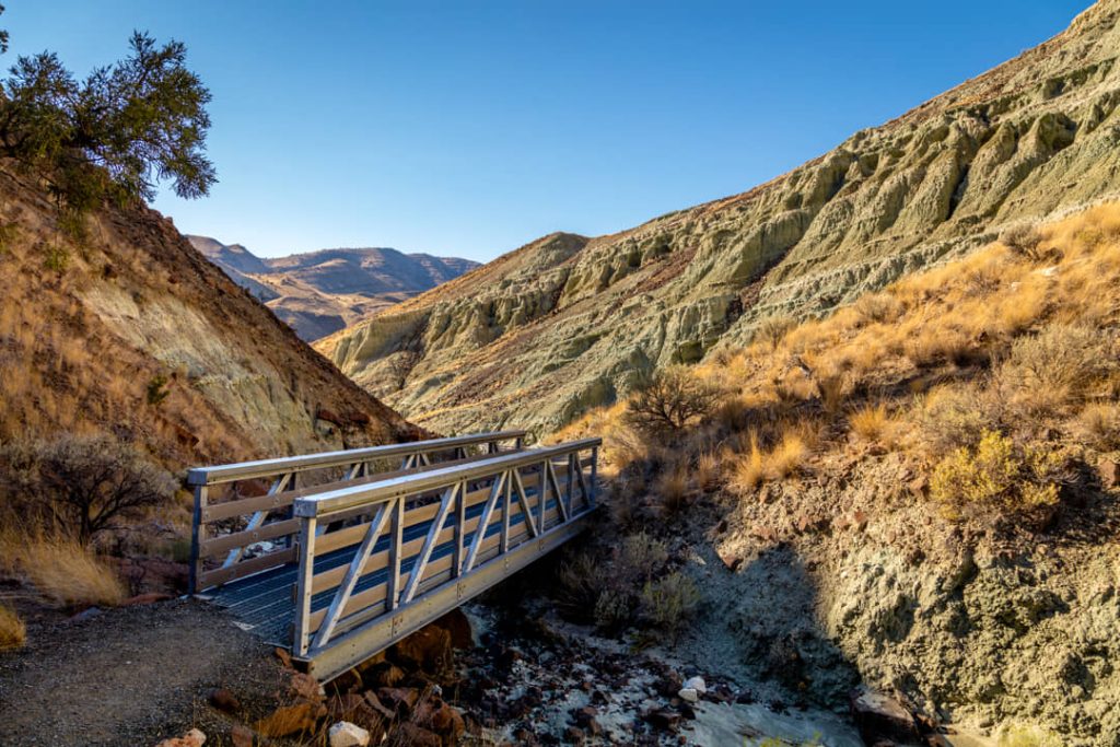 Smalle houten voetgangersbrug over een droog beekje tussen bleekgroene rotswanden in de Blue Basin kloof