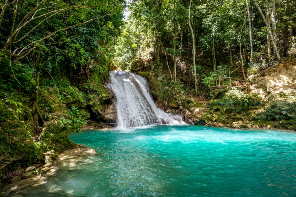 Water stroomt over rotsen in een turkooizen poel omringd door dichte jungle bij Blue Hole in Jamaica