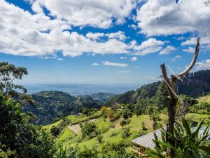 Glooiende groene heuvels van de Blue Mountains dalen af naar de kust en de zee in de verte onder een wolkenlucht in Jamaica