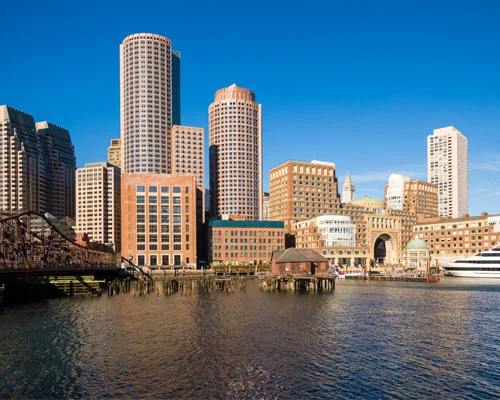 Rij bruine stadswoningen met stoepen en trappen, met roze bloesembomen ervoor in de wijk Back Bay in Boston