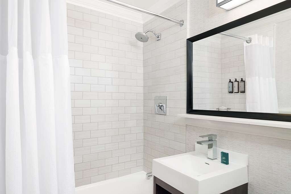 Moderne hotelbadkamer met een gestreepte douchewand, een grote spiegel en een witte wastafel met kastje in Boston