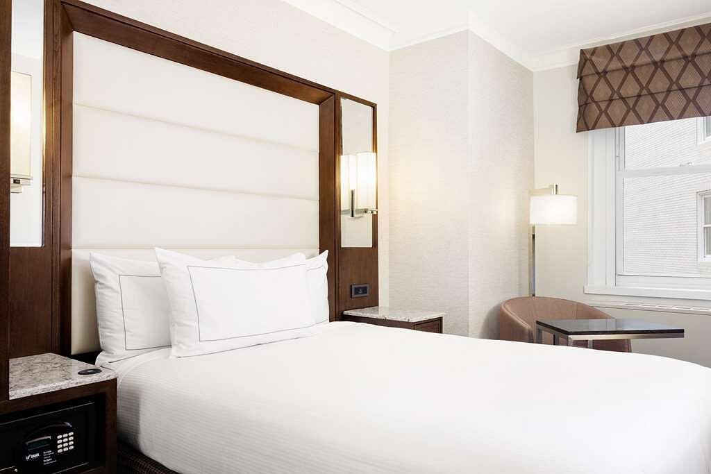 Hotelkamer met een groot bed met witte lakens onder een donker houten hemelconstructie en een bureau bij het raam in Boston