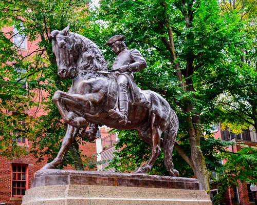 Hoge natuurstenen kerktoren met een spits naast een kerkgebouw met groen koperen dak tegen een blauwe lucht met wolken in Boston