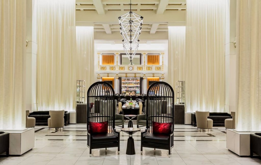 Ruime hotellobby met hoge gordijnen, een kroonluchter en opvallende zwarte kooivormige loungestoelen met rode kussens in het Hilton Boston Park Plaza