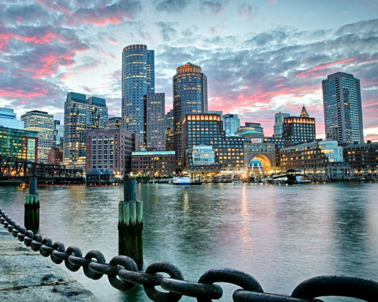 De skyline van Boston met verlichte wolkenkrabbers weerspiegelt in het water onder een roze bewolkte avondlucht