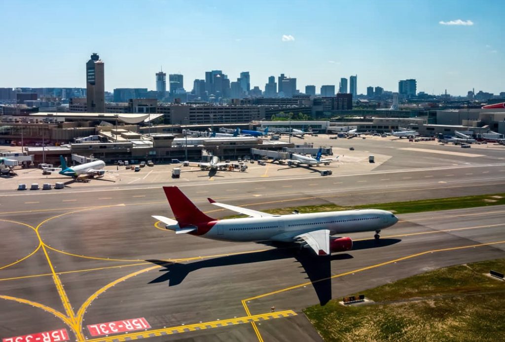 Passagiersvliegtuig taxiet over de landingsbaan van Logan Airport met de skyline van Boston zichtbaar op de achtergrond