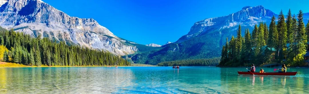 Een rode kano met kanoërs vaart over een turquoise meer omringd door dennenbossen en besneeuwde bergtoppen in British Columbia