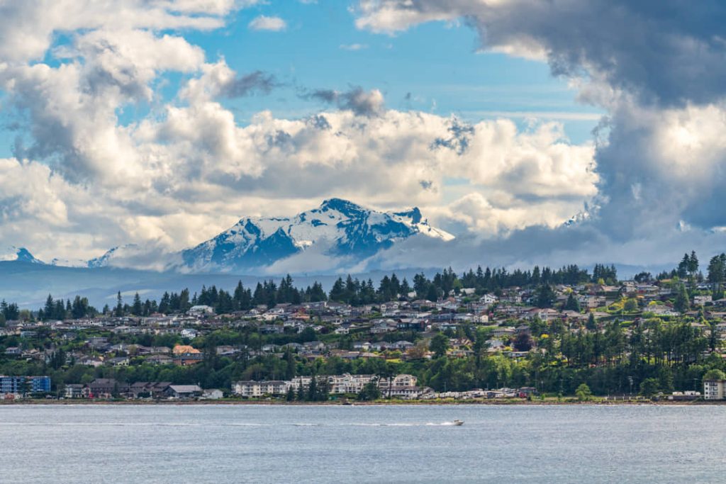 Huizen aan het water van een kustplaatsje, met wolken rond een besneeuwde bergtop en een bootje op zee in British Columbia