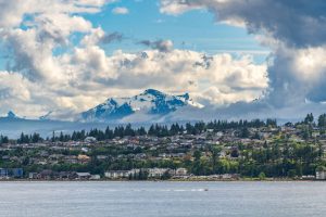 Huizen aan het water van een kustplaatsje, met wolken rond een besneeuwde bergtop en een bootje op zee in British Columbia