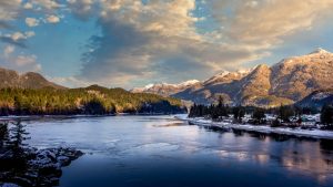 Rustige rivier weerspiegelt besneeuwde bergtoppen onder een wolkenlucht die oranje kleurt door het avondlicht in Brits-Columbia
