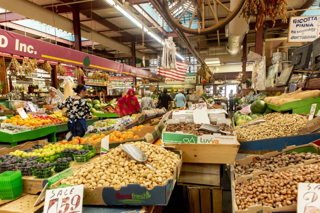 Volle marktkramen met vers fruit, groenten en noten onder een Amerikaanse vlag in de overdekte Arthur Avenue Retail Market