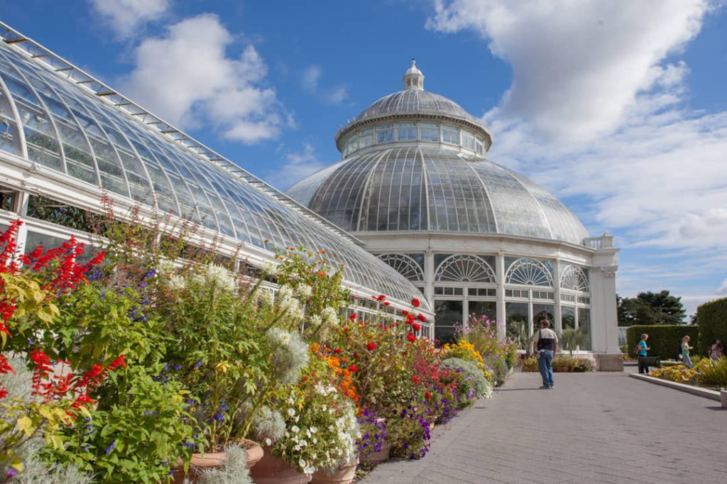 Koepelvormige Victoriaanse glazen kas met bloeiende bloembedden ervoor en bezoekers op het pad in de New York Botanical Garden