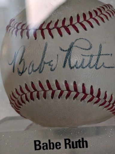 Close-up van een witte honkbal met rode stiksels en de handtekening van Babe Ruth erop in een museumvitrine