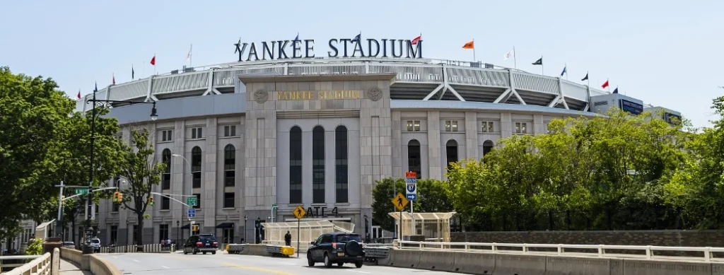 Stenen gevel met de tekst Yankee Stadium en vlaggenmasten boven de hoofdingang met verkeer op de brug ervoor