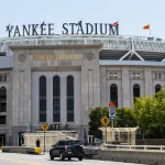 Stenen gevel met de tekst Yankee Stadium en vlaggenmasten boven de hoofdingang met verkeer op de brug ervoor